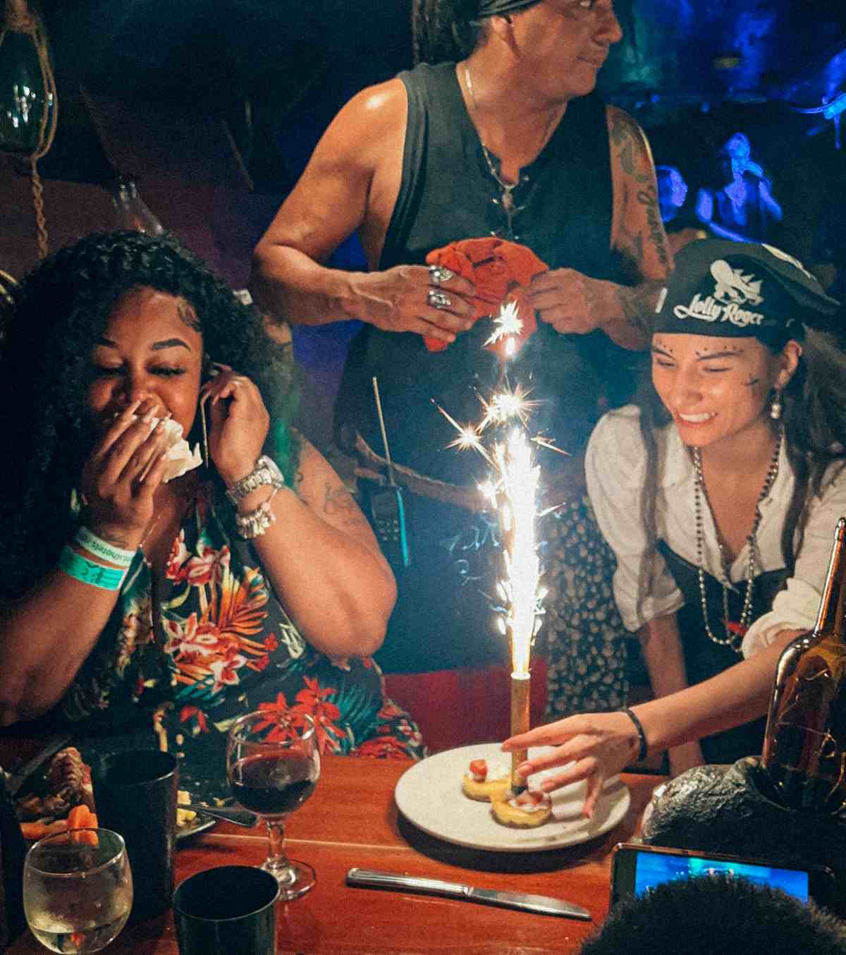 A group of people celebrating with a cake and a candle aboard the Jolly Roger pirate ship